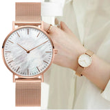 Rose gold mesh watch with pale pearl dial worn on a wrist with a white sleeve