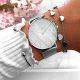 Rose gold mesh watch with white pearl dial worn on a wrist with pink blossom behind