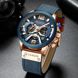 Rose gold watch with blue dial and brown leather strap shown at an angle on grey