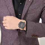 Man in a burgundy jacket wearing a black military style watch with tan strap