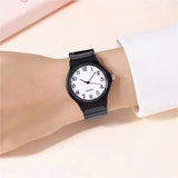 Black minimalist watch with white dial worn on wrist with white sleeve