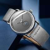 Grey dial watch with gray leather strap worn on wrist with a blue sleeve