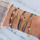 Navy cord and gold bracelet stack with flamingo charm worn on a wrist
