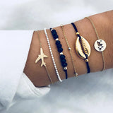 Navy cord and gold bracelet stack with shell charm worn on a wrist