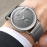 Grey dial minimalist watch worn on a wrist with a dark suit sleeve