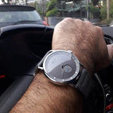 Minimalist grey dial watch worn on a wrist outdoors with buildings behind