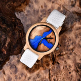 Wooden watch with blue dial and white strap resting on tree bark