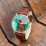 Wooden watch with teal dial and brown leather strap on wooden background