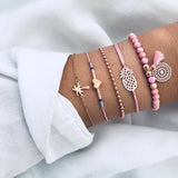 Pink bead and gold chain bracelet stack with small charms worn on a wrist