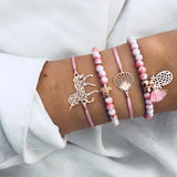 Pink bead and gold chain bracelet stack with small charms worn on a wrist