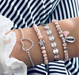 Pink bead and silver bracelet stack with elongated charm against a striped background