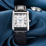 Rose gold rectangular watch with brown leather strap and white dial on blue fabric