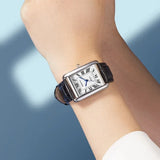 Person wearing the rectangular watch with leather strap against a light blue background
