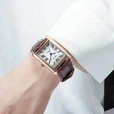 Person in a white sleeve wearing the rose gold rectangular watch with brown leather strap