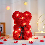Front view of red rose flower teddy bear with LED lights and rose petals scattered below