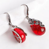 Pair of silver drop earrings with deep red teardrop stones on a pale background