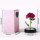 Pink and red foil rose in a lit glass dome on a black base with a book beneath