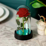 Red foil rose in a glass dome with LED lights on a dark base beside a woven basket