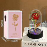 Red foil rose in a glass dome on a black base beside a book and pink backdrop