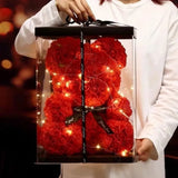 Person holding red rose flower teddy bear with LED lights in a clear gift box