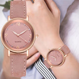 Rose gold women's watch with pink dial and dusty pink strap worn on a wrist