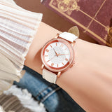 Rose gold watch with pale dial and white strap on a soft fabric surface