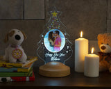Round etched photo night light on wooden base beside lit candles and a small tree