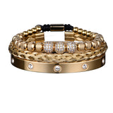 Gold three piece bracelet stack with crystal charm and Roman numeral bar on white background