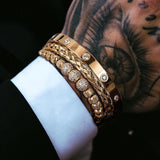 Gold three piece bracelet stack with crystal charm worn on tattooed wrist with white sleeve