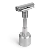 Chrome double edge safety razor standing on weighted round base against white background