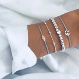 Fine silver chain bracelet stack with delicate charms against a white sleeve