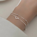 Fine silver double chain bracelet with open heart pendant worn on a wrist