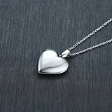 Polished silver heart photo locket on a chain against a dark slate background