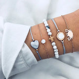 Layered silver bracelet stack with heart and disc charms on a wrist