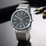 Silver mesh watch with grey dial and thin silver hands on a dark surface
