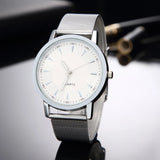 Silver mesh strap watch with white dial photographed at an angle on dark glass
