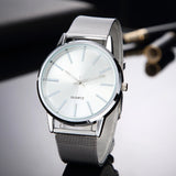 Silver mesh strap watch with white dial and slim baton markers on a dark surface