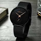 Black mesh band watch with black dial shown at an angled view on wood