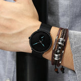 Black mesh band watch worn on wrist paired with a beaded bracelet