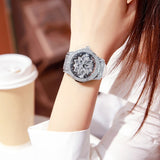 Silver crystal snowflake dial watch with white strap worn on a wrist beside a coffee cup