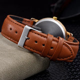 Art dial watch with brown leather strap coiled to show smooth steel caseback and buckle
