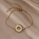 Gold sunburst charm bracelet on soft cream fabric showing fine chain links