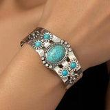 Silver cuff bracelet set with turquoise stones worn on a wrist against dark clothing