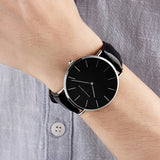 Black dial minimalist watch with black leather strap worn on wrist with denim sleeve
