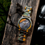 Multicolor camouflage wooden watch resting on a wooden log outdoors