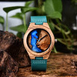 Wooden watch with teal dial and brown leather strap resting on tree bark