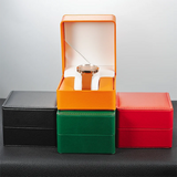 Orange PU leather watch case open displaying a brown leather strap watch on a stand