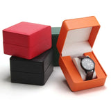 Stacked PU leather watch storage boxes in red, black, green, and orange with one open showing a watch
