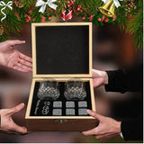Person presenting open whiskey stones gift box with glasses and stones, holiday decor behind