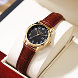 Gold case women's watch with black dial and deep red leather strap on a wrist